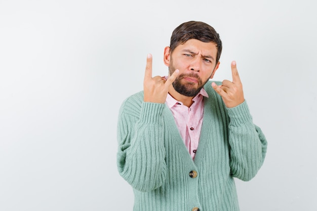 Young male doing rock symbol in shirt, cardigan and looking confident , front view.