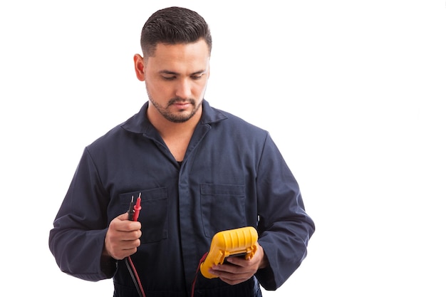 Young male electrician checking voltage using a multimeter on a white background