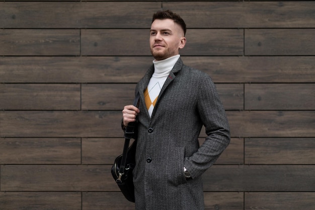 A young male entrepreneur with a business black bag on his shoulder stands against a brown wall