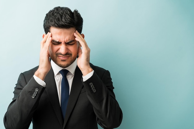 Young male executive grimacing from headache against isolated background