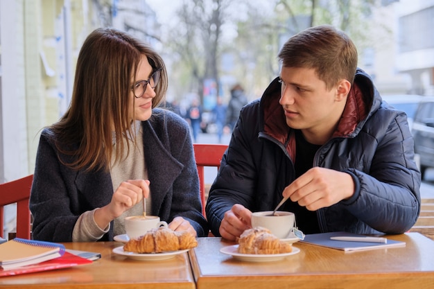 Young male and female friends students sitting in outdoor cafe