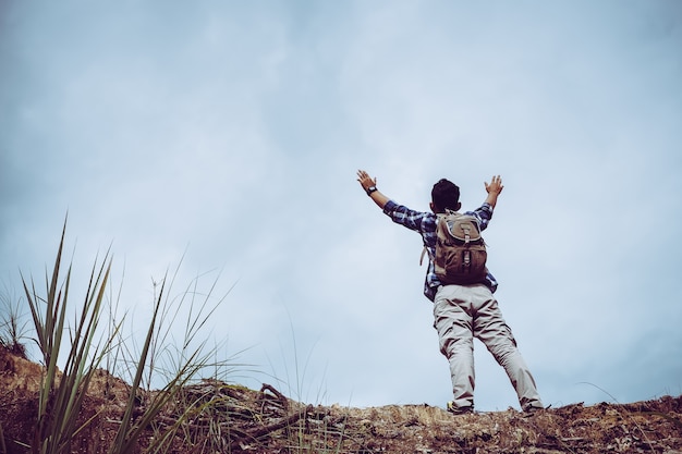 Young male hiker with backpack reaching up top of mountain and raised hands