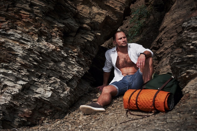 Young male hiker with backpack relaxing on a rocky massif during calm summer sunset. Travel Lifestyle adventure vacations concept