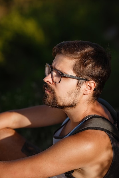 Young male hiker with backpack relaxing on top of a mountain during calm summer sunset