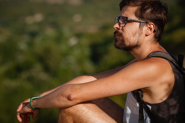 Young male hiker with backpack relaxing on top of a mountain during calm summer sunset