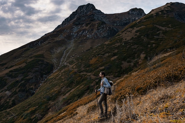 Young male hipster in the mountains in autumn. Discovery Travel Destination Concept. Tourist on the high rocks background. Sport and active life concept.