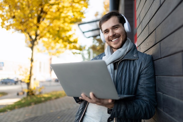 A young male it worker works on a laptop and listens to music on headphones in my office with a wide