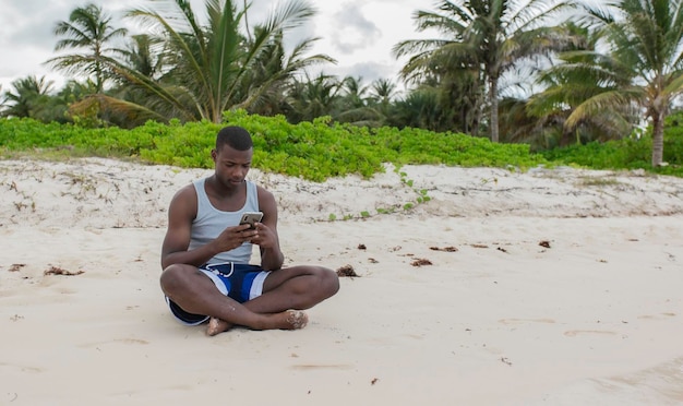 Young male man using smartphone sitting on the beach sand