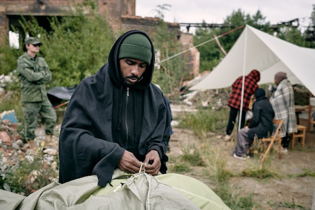 Photo young male migrant pitching tent in refugee camping