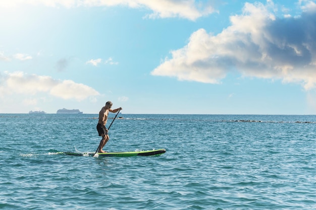 Young male surfer riding standup paddleboard in ocean