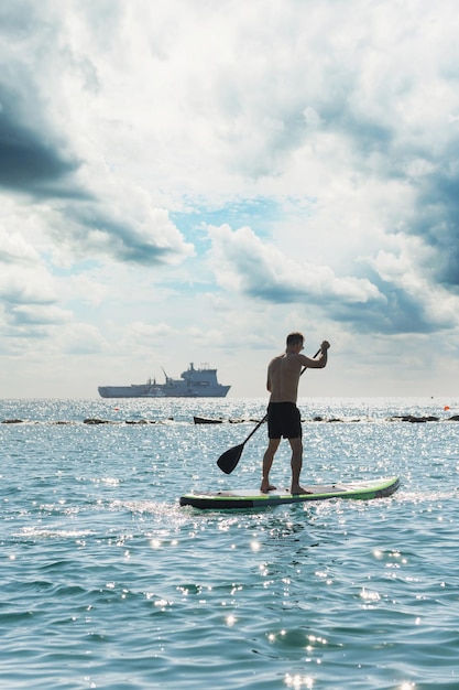 Young male surfer riding standup paddleboard in ocean