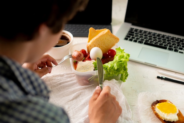 Photo young male taking meal in front of the laptop while working, bad habit and obesity concepts