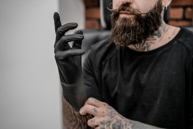 Young male tattoo artist with beard holding pencil and sketch looking positive and happy standing and smiling in workshop place.