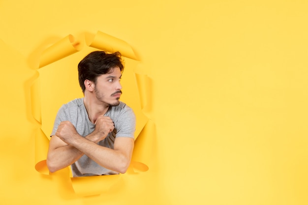 young male trying to get out from torn yellow paper background guy handsome facial