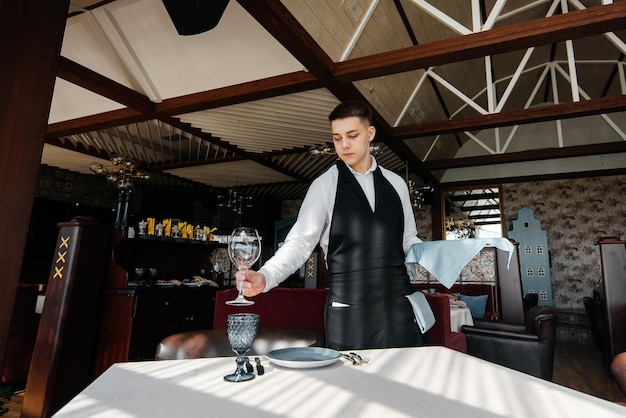 A young male waiter in a stylish uniform is engaged in serving the table in a beautiful gourmet restaurant A highlevel restaurant Table service in the restaurant