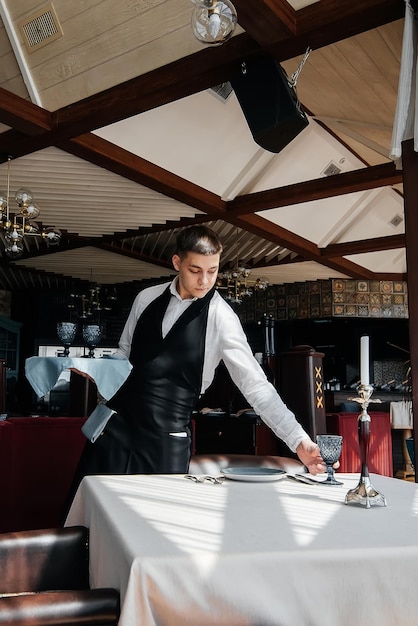 A young male waiter in a stylish uniform is engaged in serving the table in a beautiful gourmet restaurant A highlevel restaurant Table service in the restaurant