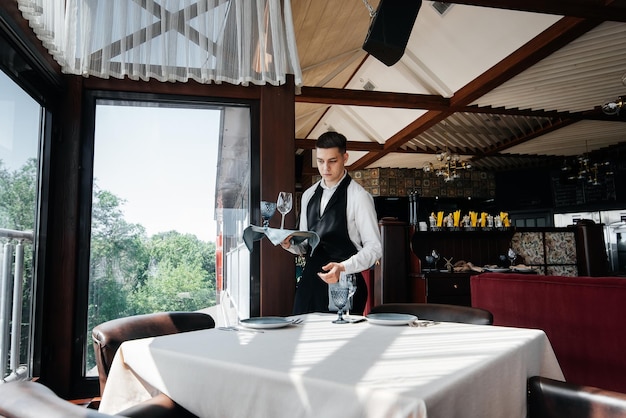 A young male waiter in a stylish uniform is engaged in serving the table in a beautiful gourmet restaurant A highlevel restaurant Table service in the restaurant