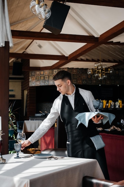 A young male waiter in a stylish uniform is engaged in serving the table in a beautiful gourmet restaurant A highlevel restaurant Table service in the restaurant