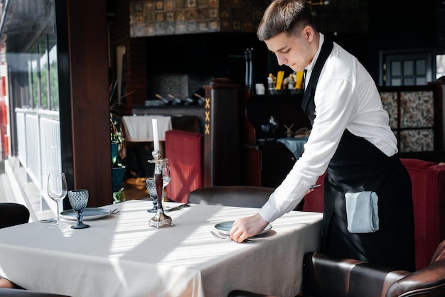 A young male waiter in a stylish uniform is engaged in serving the table in a beautiful gourmet restaurant A highlevel restaurant Table service in the restaurant