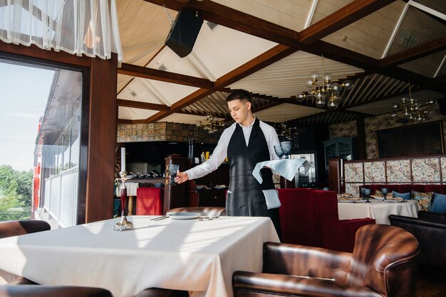 A young male waiter in a stylish uniform is engaged in serving the table in a beautiful gourmet restaurant. Restaurant activity, of the highest level.