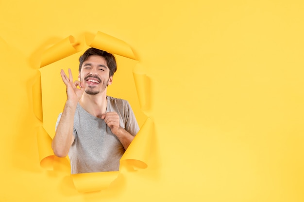 young male with winking expression on torn yellow paper background facial indoor guy handsome