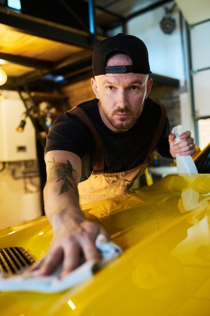 Young male worker or technician with bottle of detergent cleaning hood cover