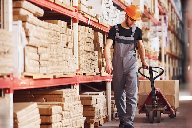 Young male worker in uniform is in the warehouse pushing pallet truck.