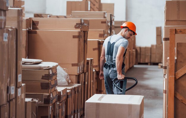 Young male worker in uniform is in the warehouse with pallet truck.