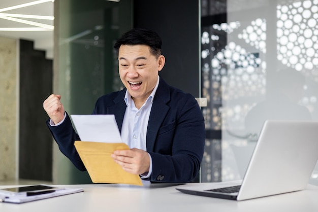 A young man an asian businessman sits smiling in the office at the table works with documents holds