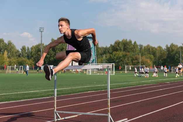 Young man athlete runnner running hurdles at the stadium outdoors