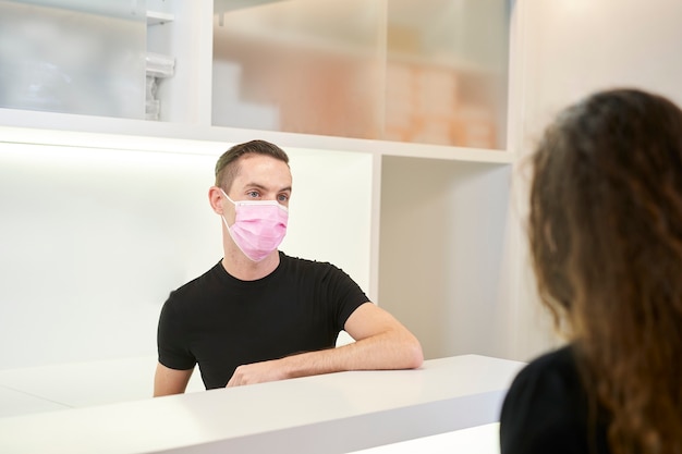 Young man attending to a client at the reception of a dental, gynocological or aesthetic clinic.