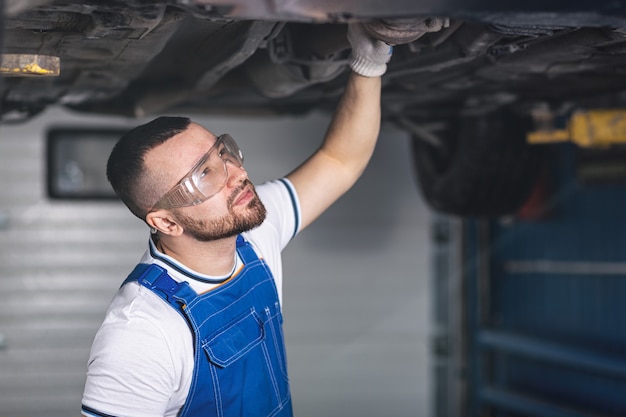 Young man auto mechanic in overalls at his workplace repairs the car's suspension