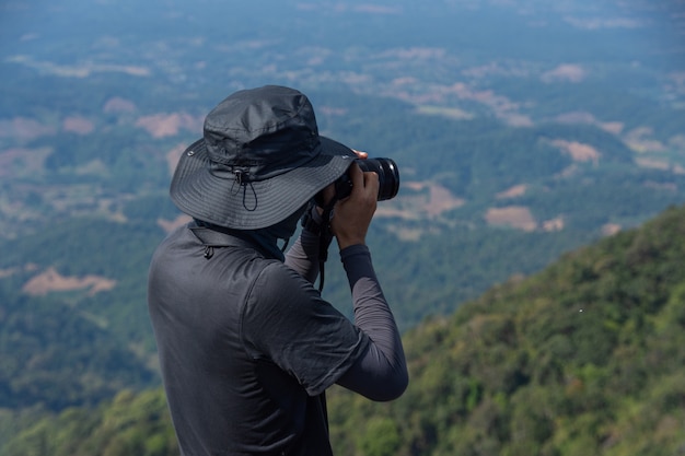 Young man backpacker hiking on mountain peak and take photo and holding camera, subject is blurred. selected focus