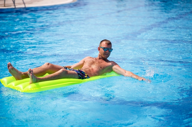 A young man bathes in the pool on a yellow inflatable mattress