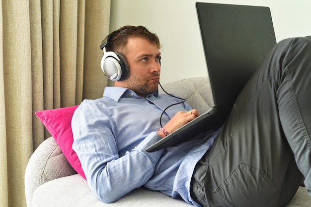 Young man beat maker working from home with his laptop laying on couch