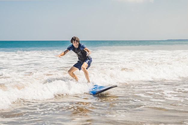 Young man beginner Surfer learns to surf on a sea foam on the Bali island