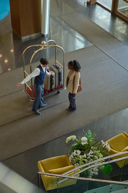 Young man in bellboy uniform showing way to hotel room to traveler