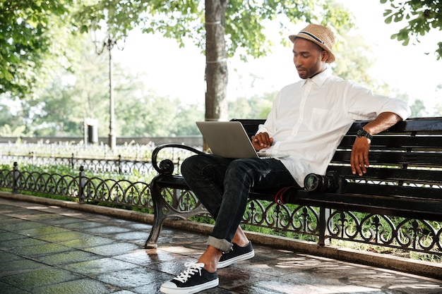 Young man on a bench with laptop and camera