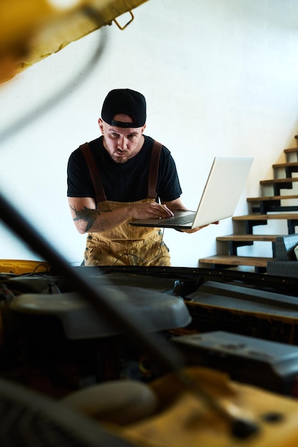 Young man bending forwards over open hood and using laptop