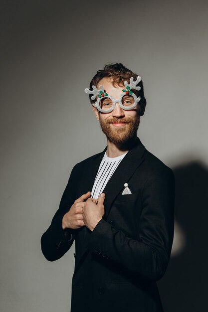 Young man in black jacket with party glasses on color background