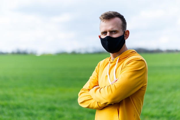 Young man in black protective antiviral mask on the street. The guy is resting in the park on a sunny summer day in a mask made by his own hands. Virus protection. Quarantine measures