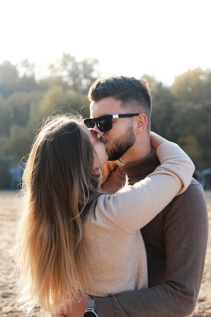 A young man in black sunglasses hugs a girl by the waist and kisses