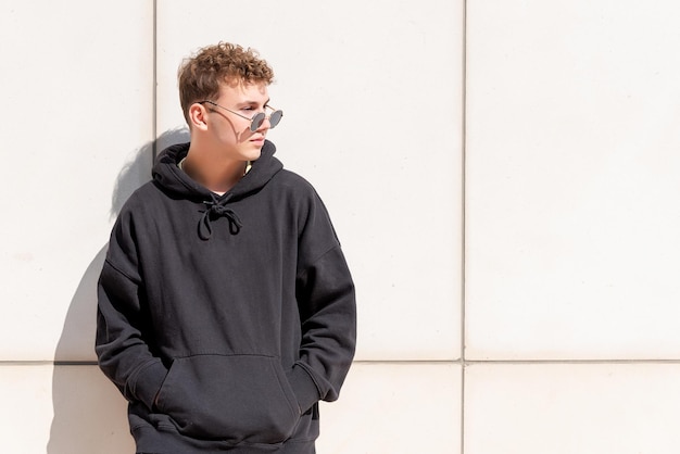 Young man in black sweatshirt posing with his sunglasses outdoors