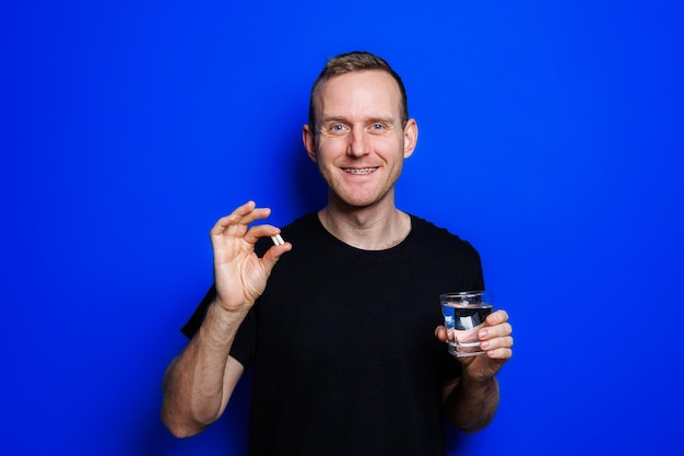 A young man in a black Tshirt on a blue background stands with a thermometer in his hands An increase in body temperature feeling sick Weakened immunity Selective focus