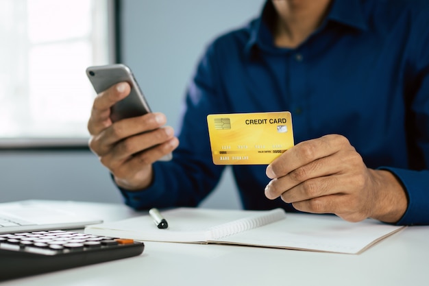 Young man in blue shirt entering security code with mobile phone and paying with credit card