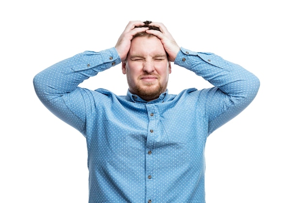 A young man in a blue shirt holds his head in displeasure Negative emotions and stress Isolated on white background