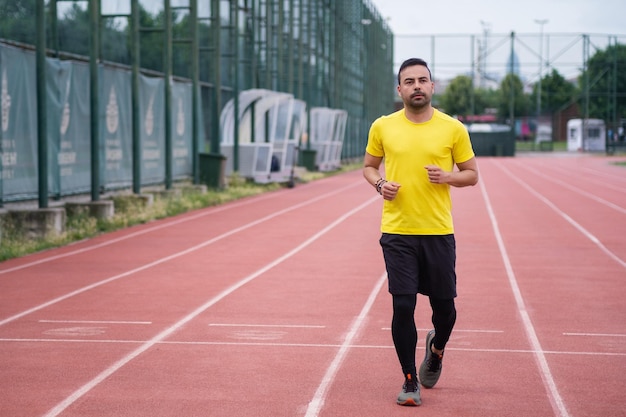 Young man in bright tshirt running along empty track with red rubber surface