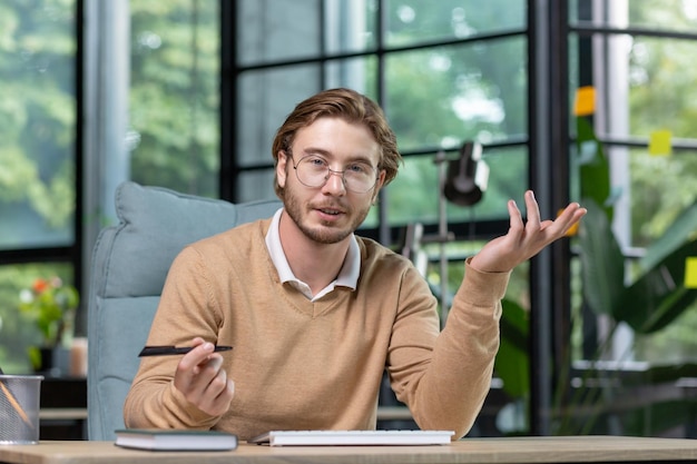 Young man businessman programmer sits in the office and chats and smiles at the camera conducts