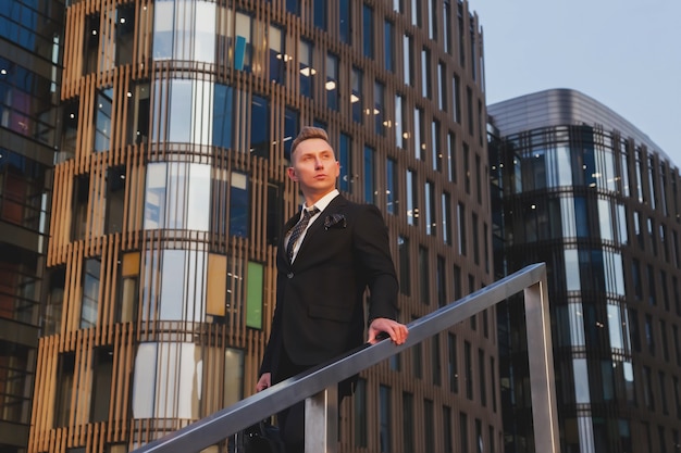 Young man businessman in style wear clothes and with briefcase leaves business building near corporate company, lifestyle