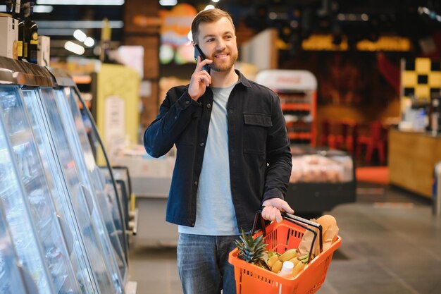 Young man buying groceries at the supermarket Other customers in background Consumerism concept